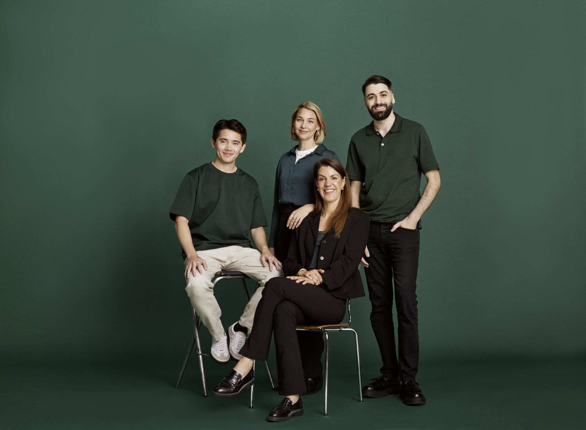 fyra personer ler mot kameran med mörkgrön bakgrund