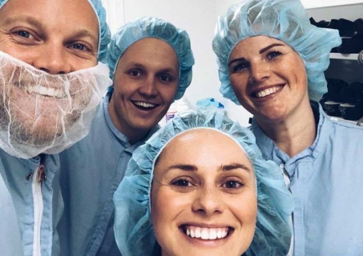 Gruppbild på nära håll av medarbetare på AztraZeneca och representater från Oddwork. Alla är klädda i ljusblå skyddskläder och skyddsmössor för håret.