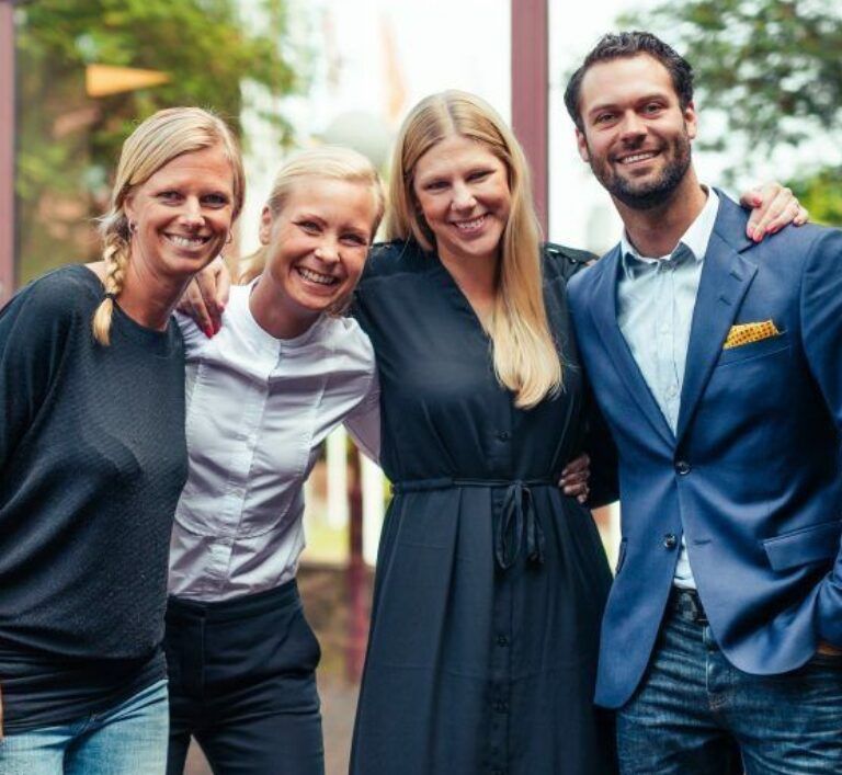 Foto på fyra medarbetare på Sector Alarm. Gruppen stå utomhus med gröna träd i bakgrunden.