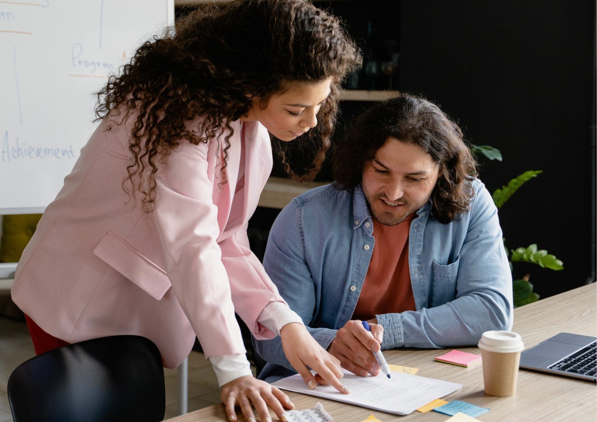 En kvinna står upp vid ett skrivbord och diskuterar med en man som sitter ner.