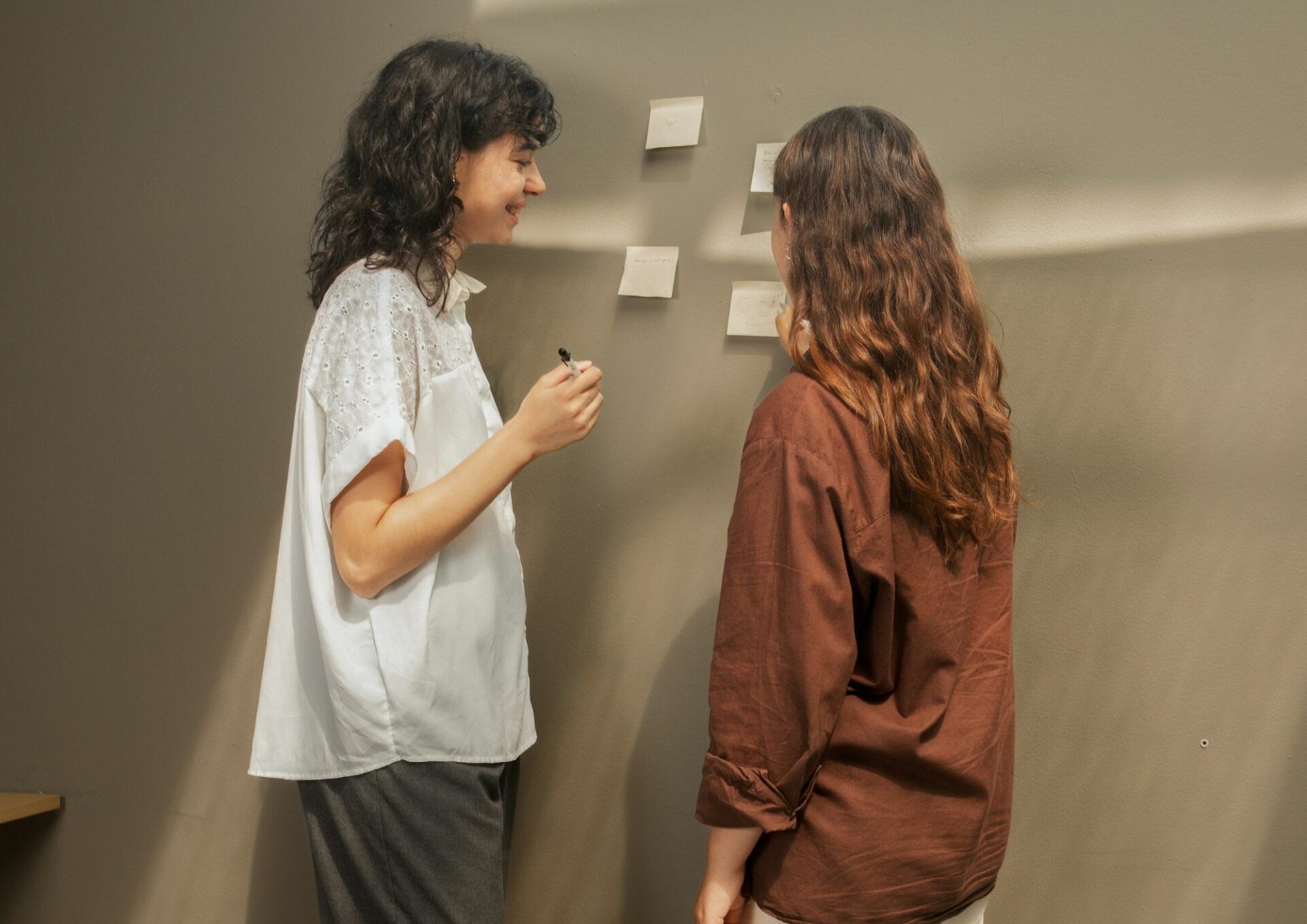 Två kvinnor står framför en whiteboard med post-it-lappar och diskuterar.