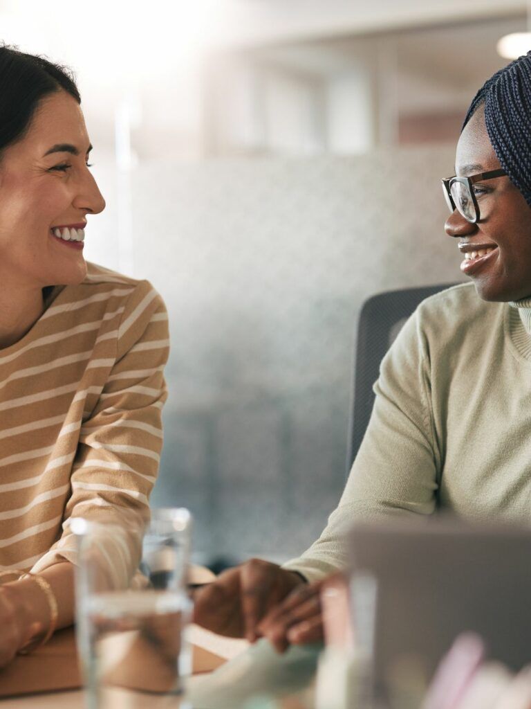 Två personer som krattar och ser på varandra medan de sitter vid ett bord i kontorsmiljö