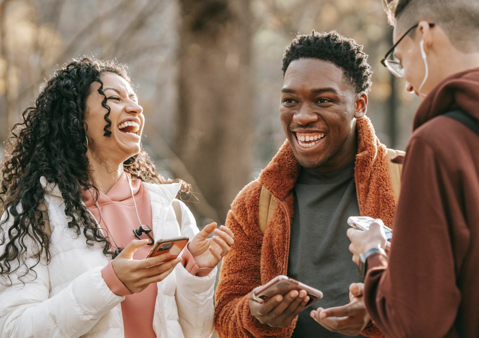 En kvinna och två män står utomhus och skrattar tillsammans.
