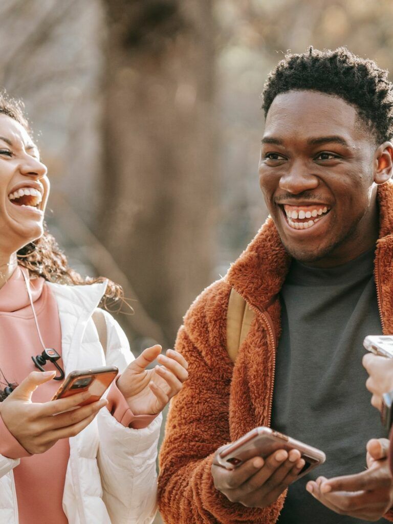 En kvinna och två män står utomhus och skrattar tillsammans.