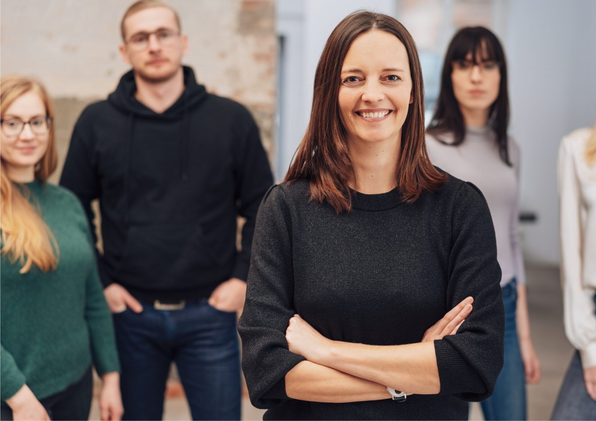 I förgrunden syns en kvinna som ler och har brunt, axellångt hår. I bakgrunden står hennes team, bestående av fyra personer. Alla är ledigt klädda och ser in i kameran.