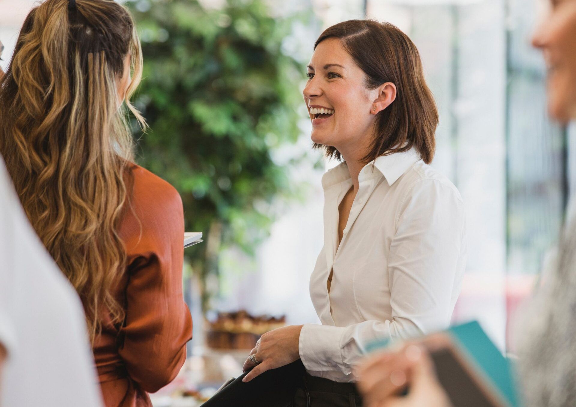 Kvinna i vit skjorta skrattar med en annan person som är vänd från kameran.