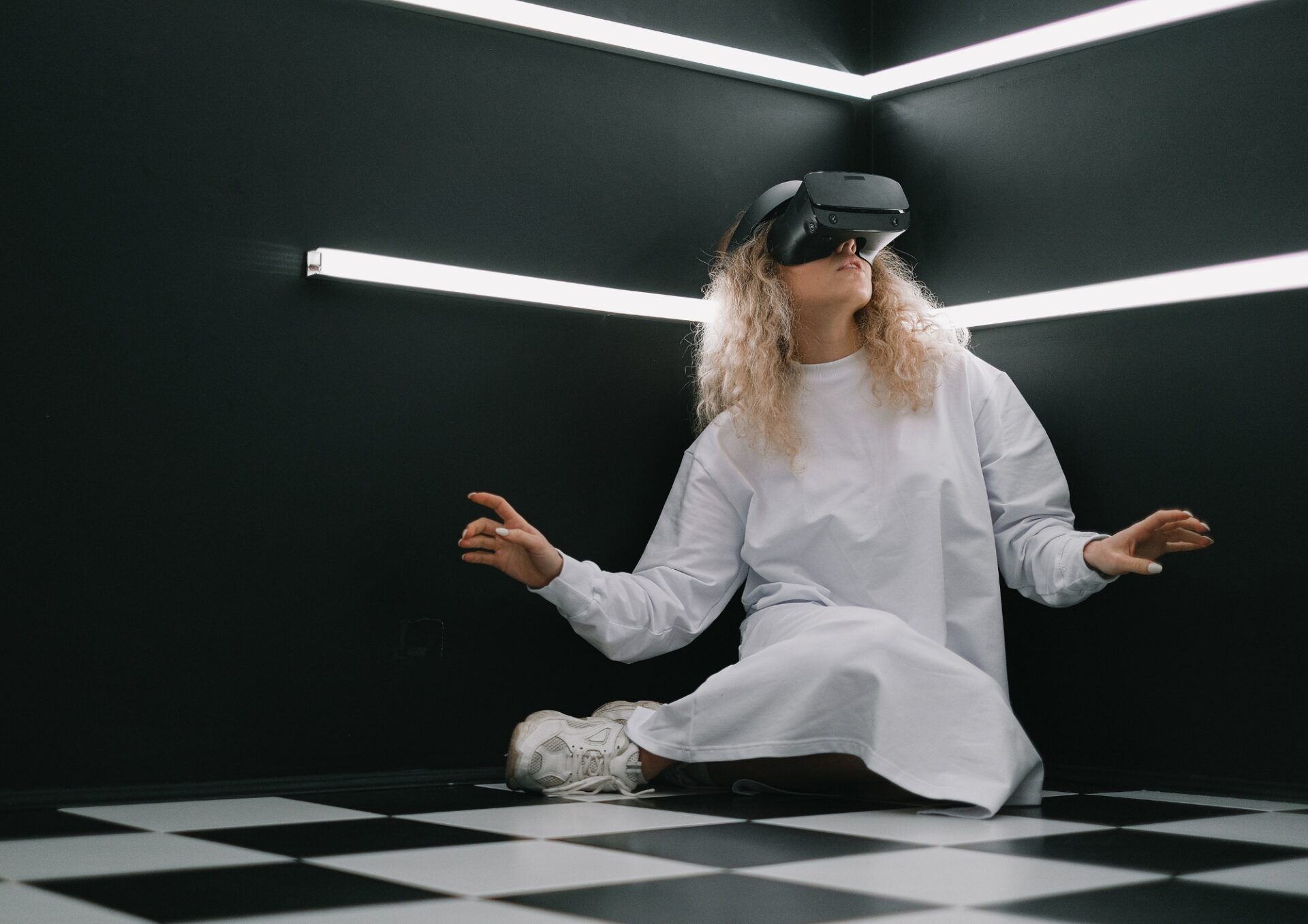 En person som sitter på ett svartvitrutigt golv. Personen har lockigt hår och bär VR-glasögon.