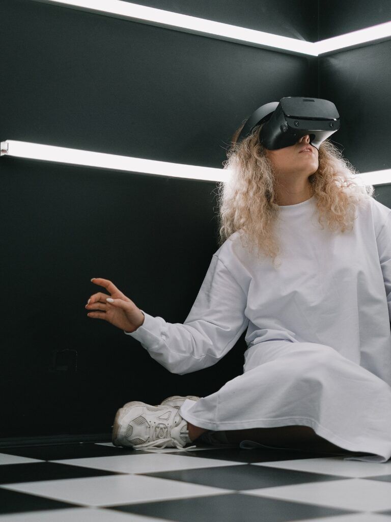 En person som sitter på ett svartvitrutigt golv. Personen har lockigt hår och bär VR-glasögon.