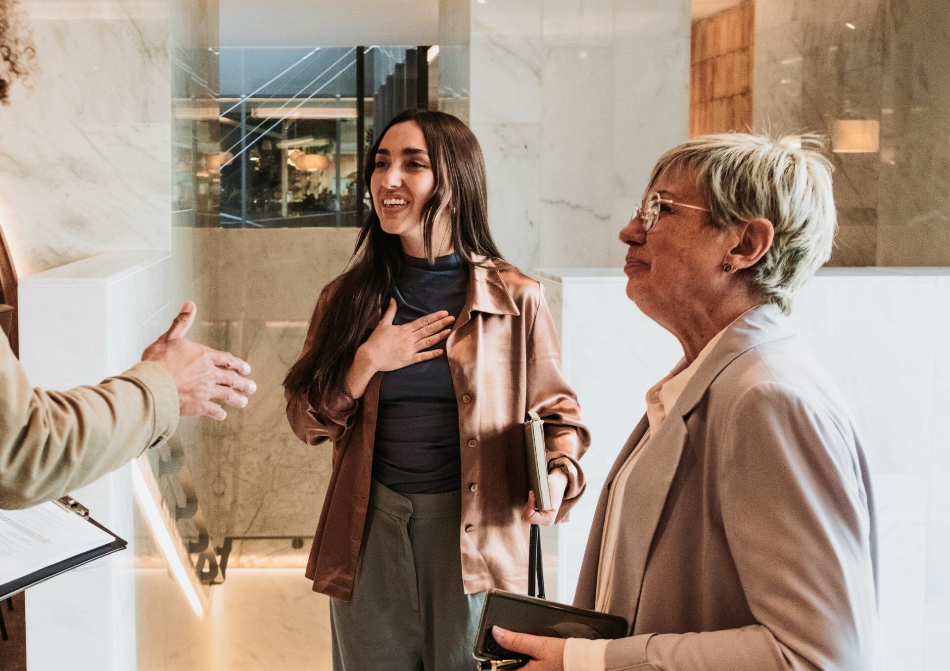 En person i vänstra kanten av bilden sträcker ut handen och välkomnar två leende kvinnor.