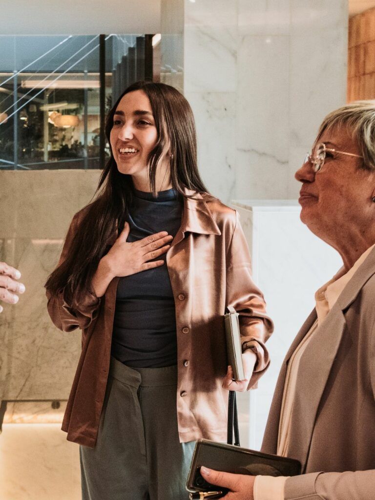 En person i vänstra kanten av bilden sträcker ut handen och välkomnar två leende kvinnor.