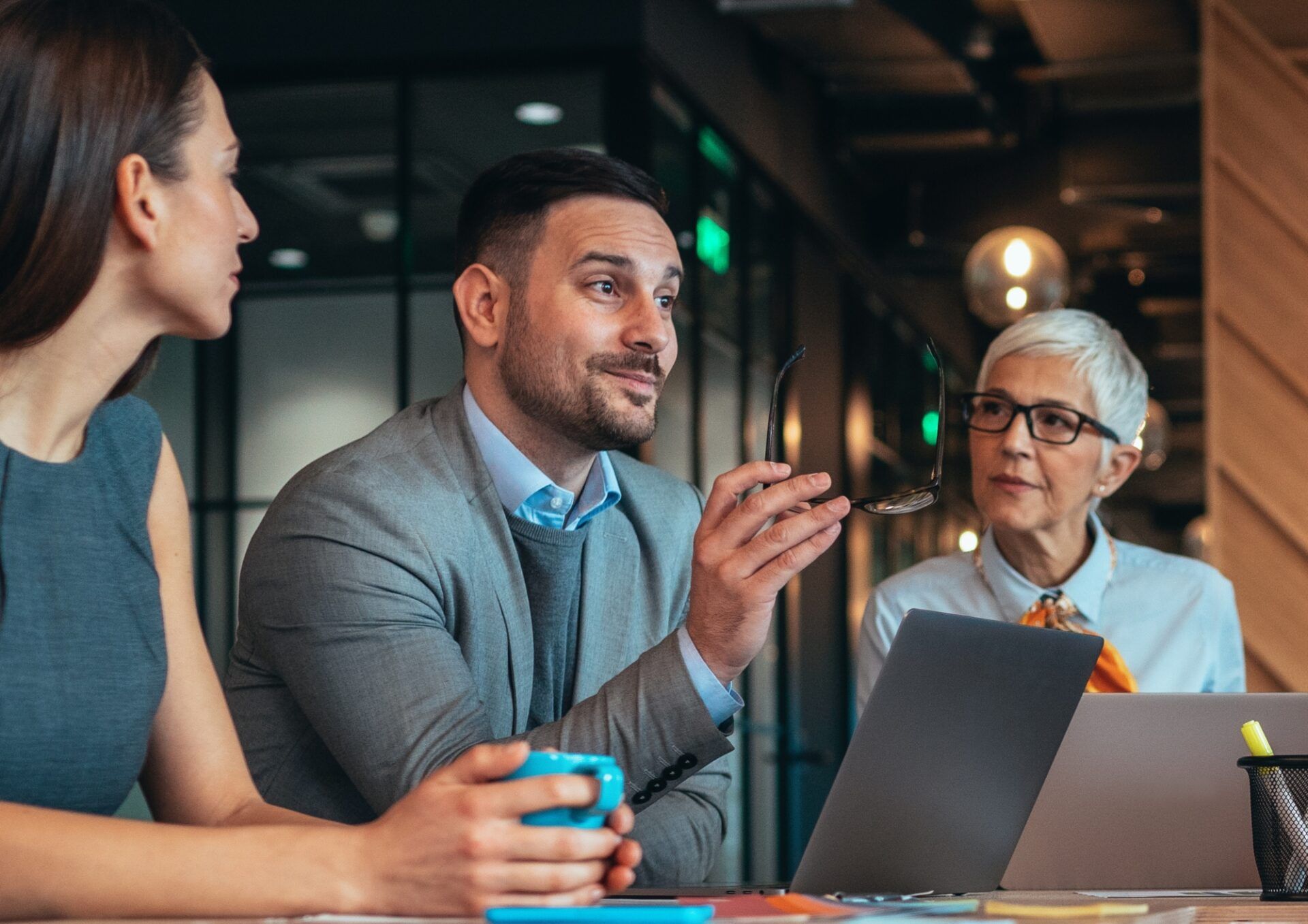 Tre personer vid ett bord sett från sidan. En har en blå mygg i händerna och de andra två sitter framför varsin laptop.