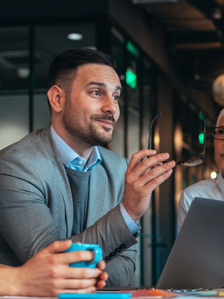 Tre personer vid ett bord sett från sidan. En har en blå mygg i händerna och de andra två sitter framför varsin laptop.