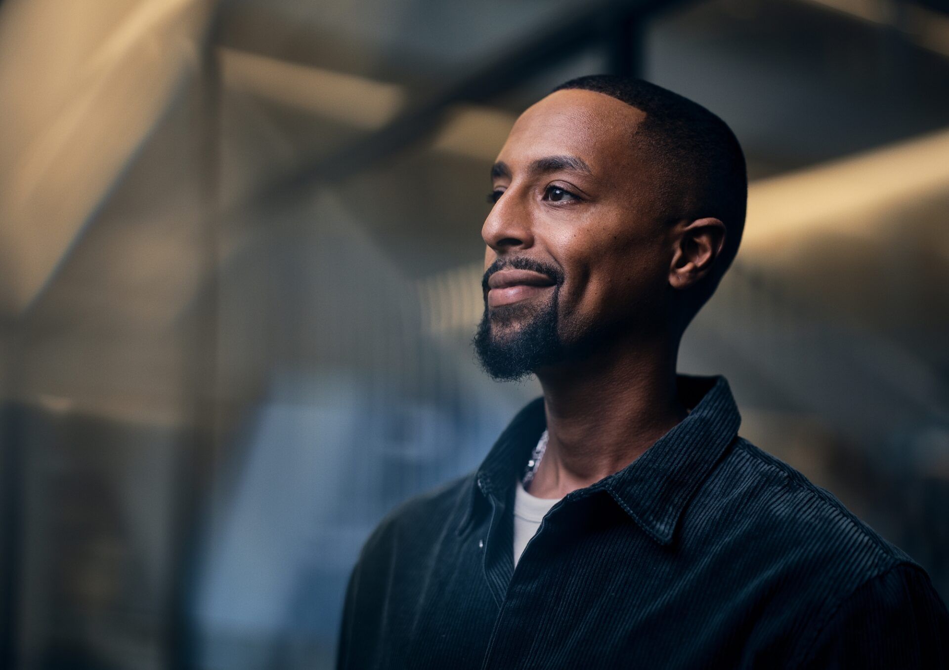 Bild på en person med mörkblå manchesterskjuorta och ett litet leende på läpparna. Bakgrunden är mörk i blåa nyanser.