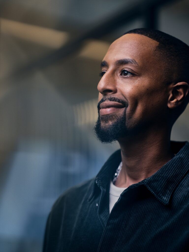 Bild på en person med mörkblå manchesterskjuorta och ett litet leende på läpparna. Bakgrunden är mörk i blåa nyanser.