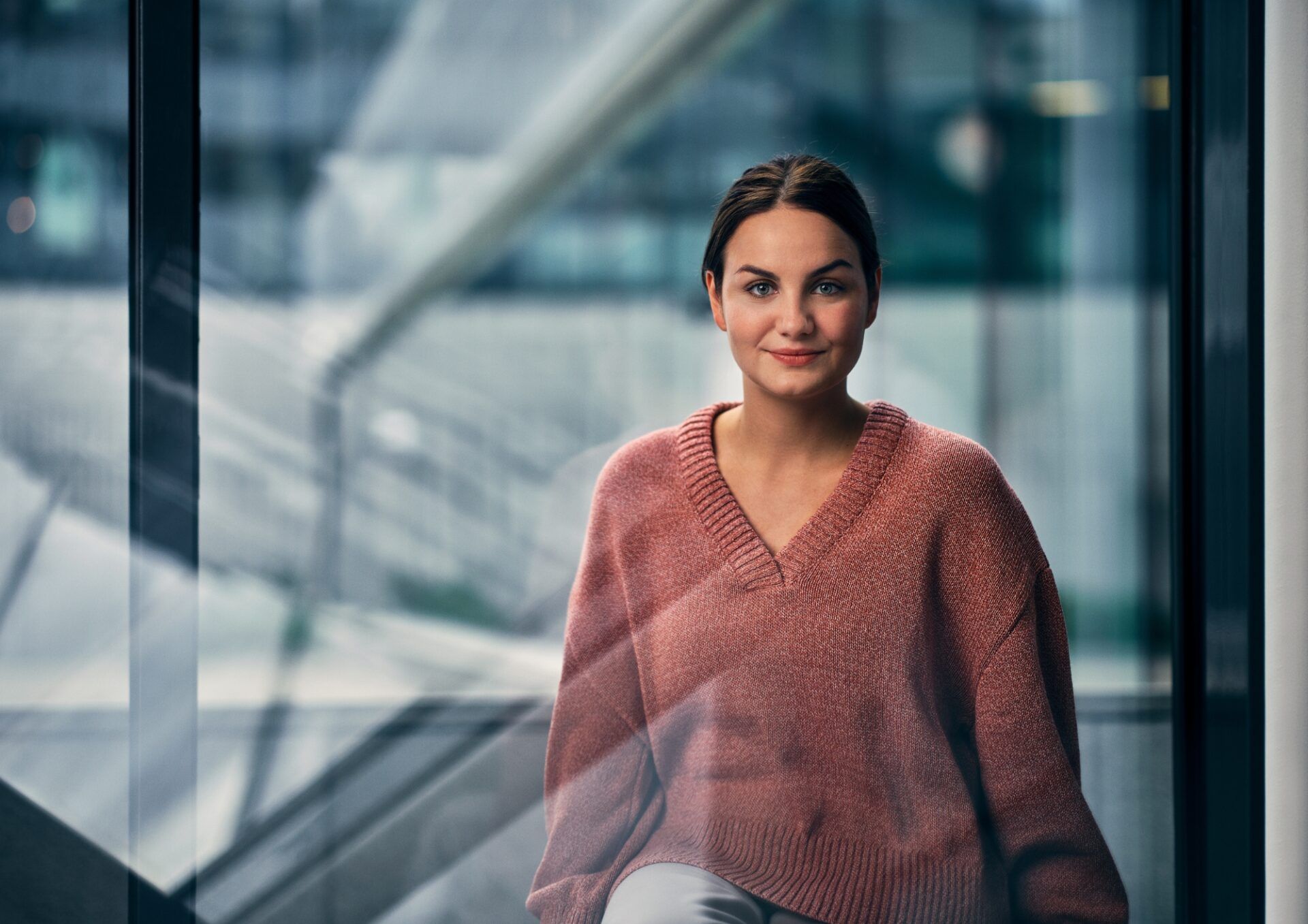 Person i mörkrosa stickad tröja som sitter vi ett fönster.