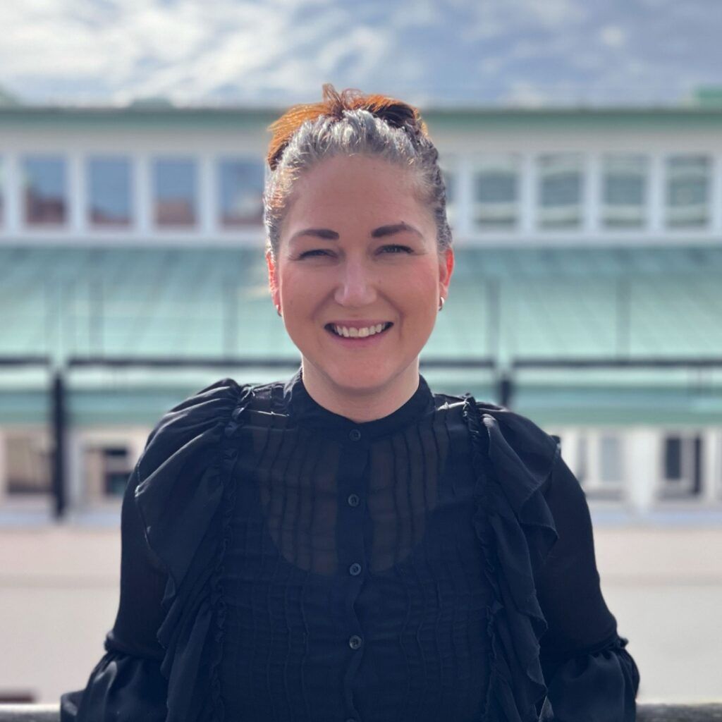 Foto på Carolina Elofsson. Carolina står på en balkong och i bakgrunden ser man hustak i grön koppar.