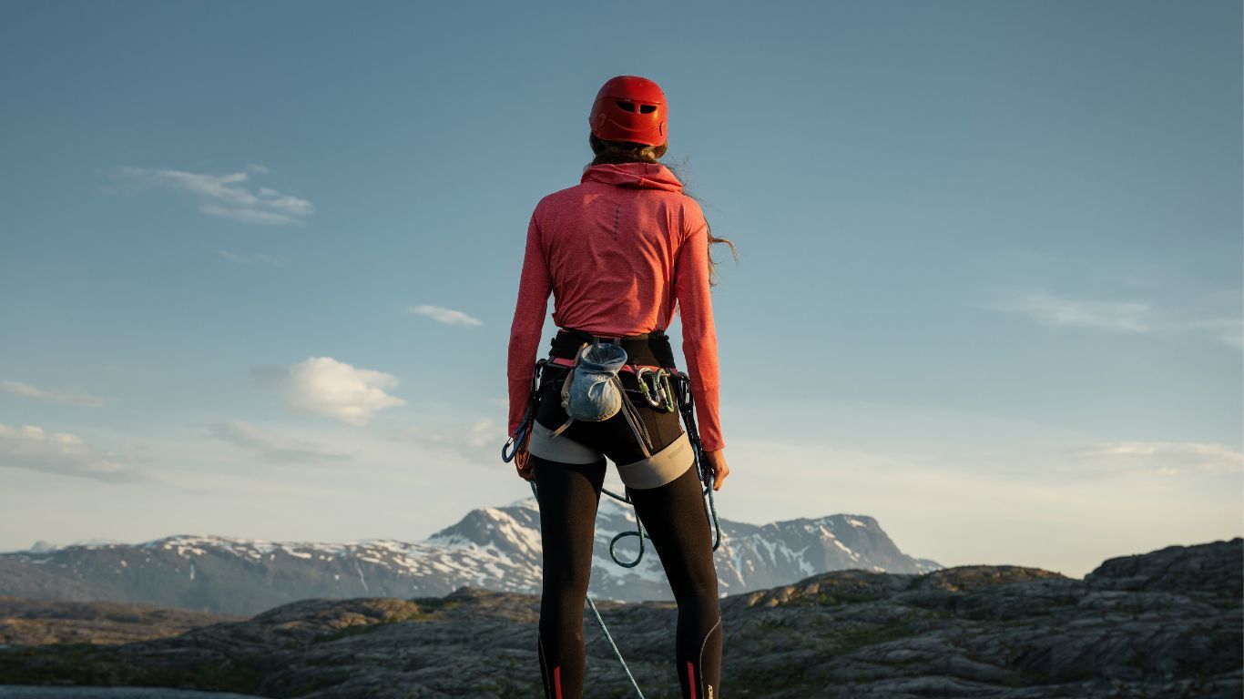 En person i klättringsutrustning står på toppen av ett berg och tittar ut över bergstopparna.