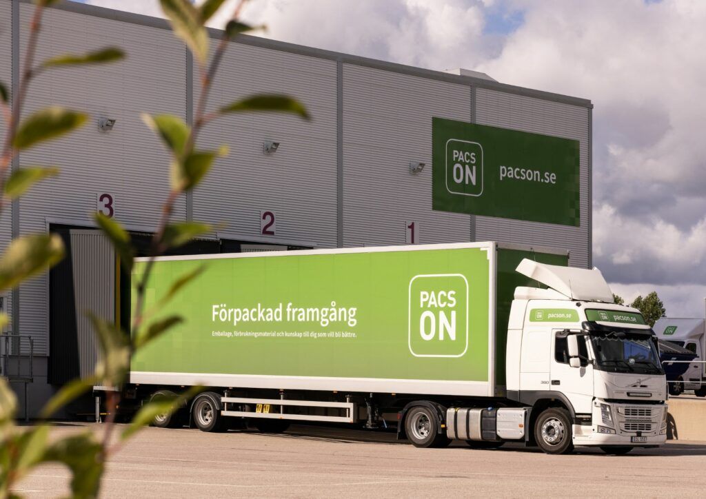 Foto på lastbil med långt täckt släp som har Pacsons branding och logga i vitt på ljusgrön bakgrund