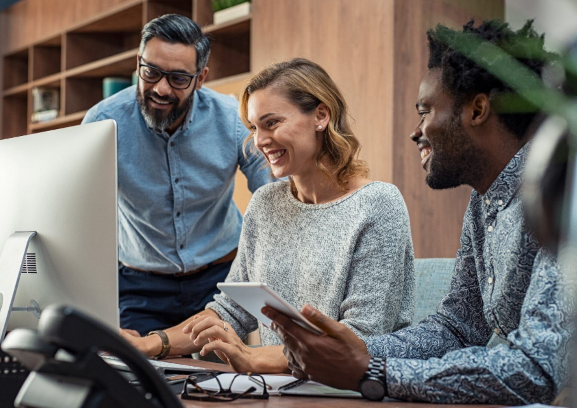 En man står upp bredvid en kvinnlig och manlig kollega som sitter ner vid en dator.