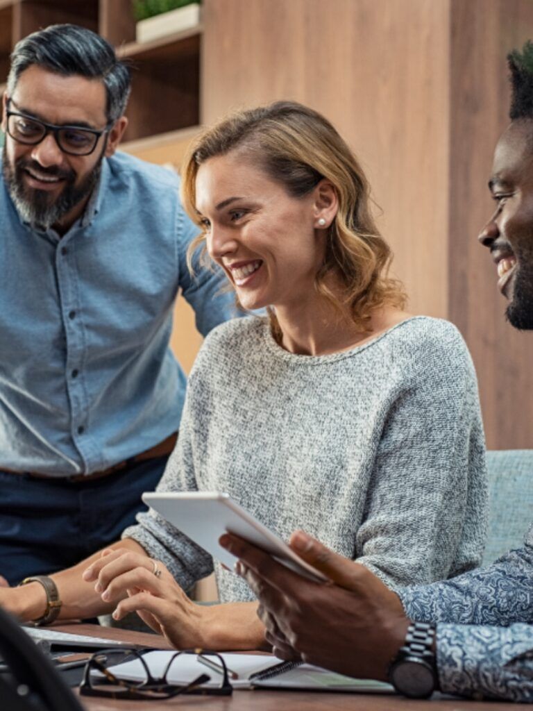 En man står upp bredvid en kvinnlig och manlig kollega som sitter ner vid en dator.