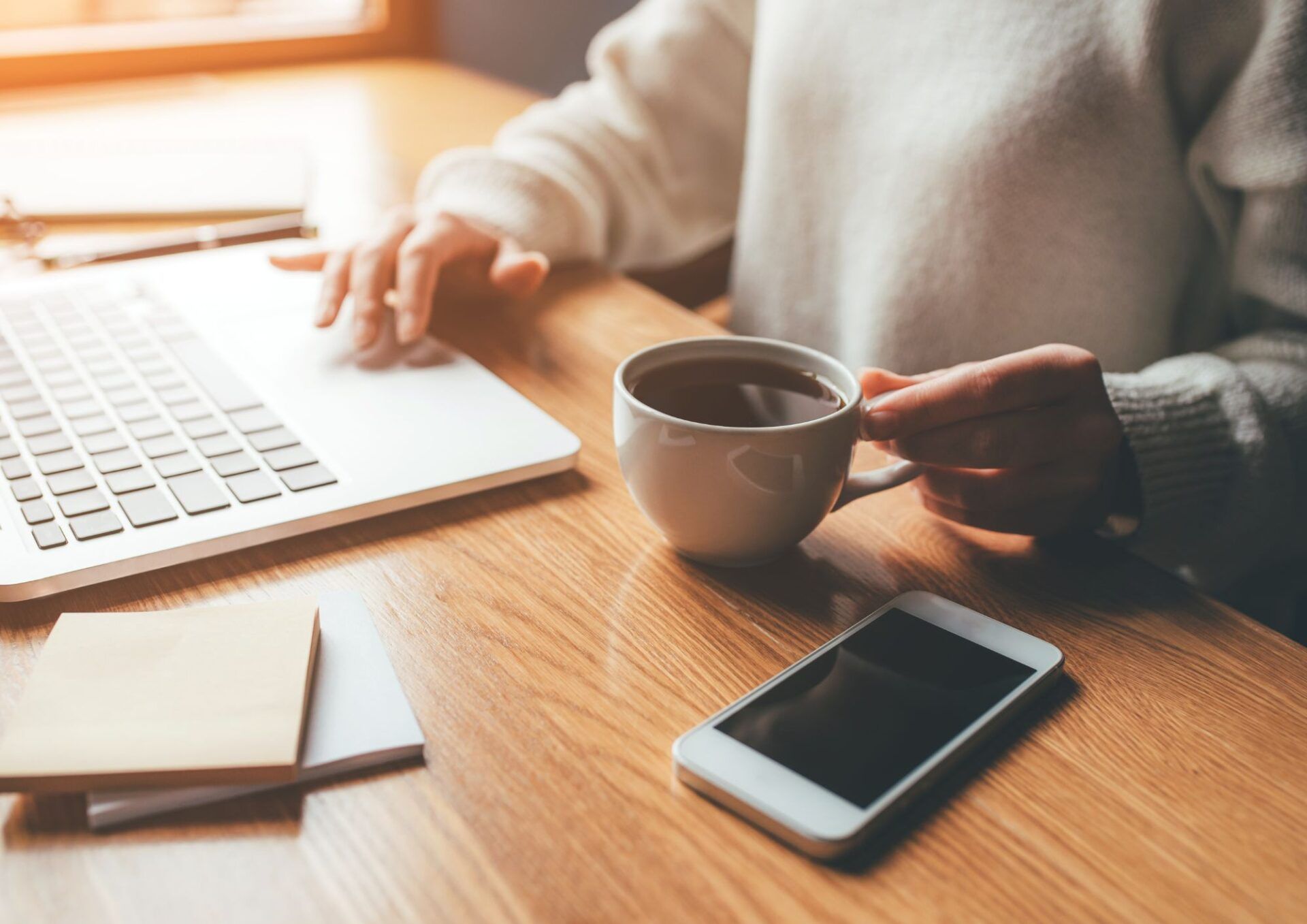 En person arbetar vid sin laptop med en kopp kaffe.