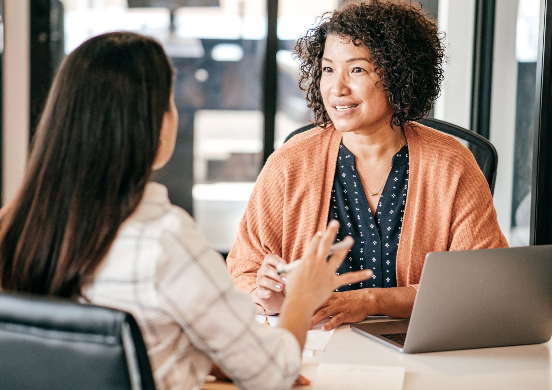Två kvinnor sitter mittemot varandra i en kontorsmiljö och samtalar. 