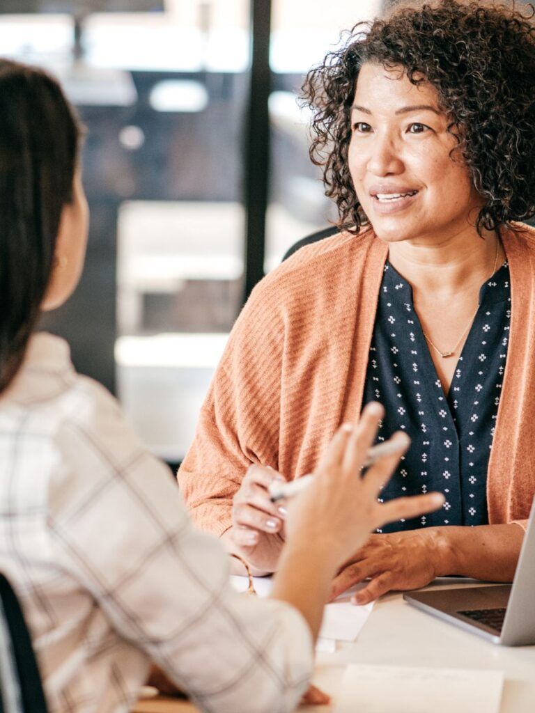 Två kvinnor sitter mittemot varandra i en kontorsmiljö och samtalar. 