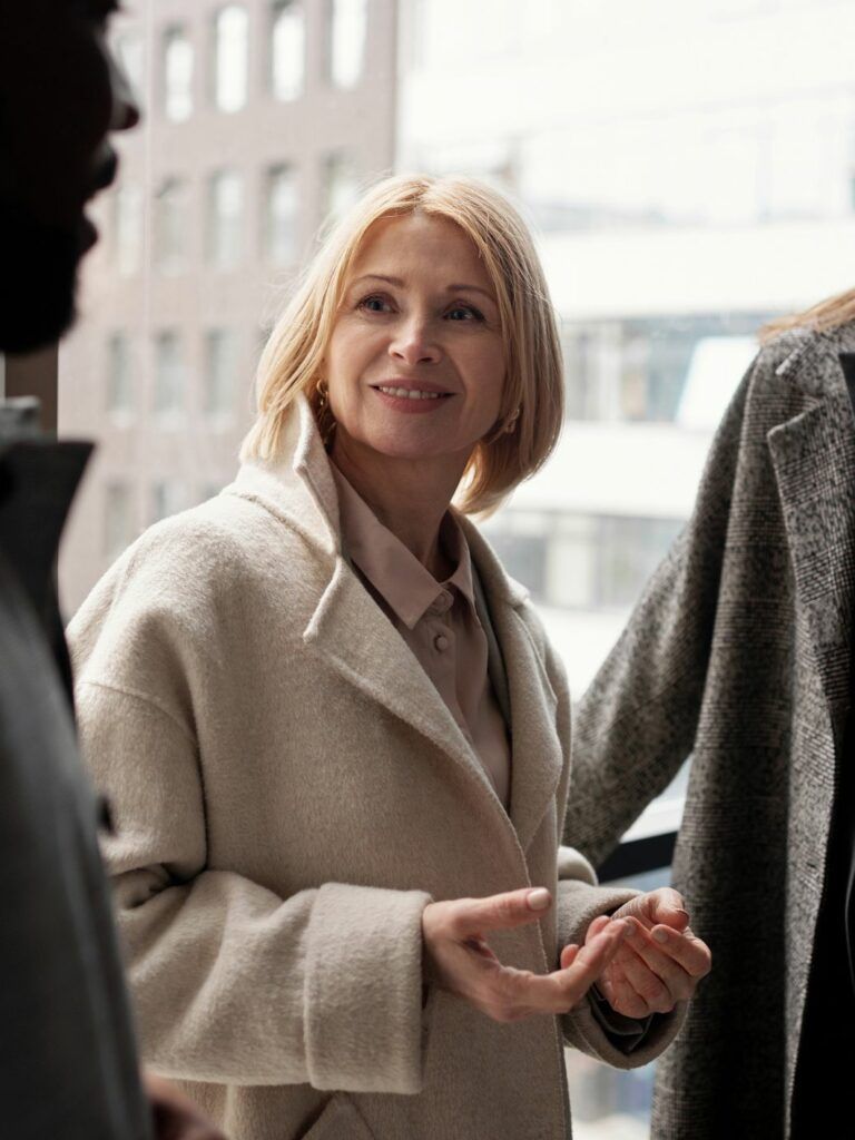 I förgrunden en person som syns suddigt, i fokus två personer i vinterkappor som ler och riktar sin uppmärksamhet mot personen i förgrunden.