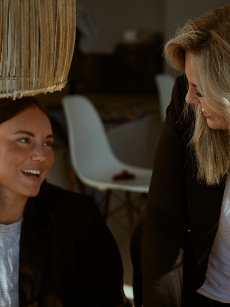 Bildpå två personer som skrattar. Personen till höger står upp och lutar sig framåt samt tittar på personen till vänster.