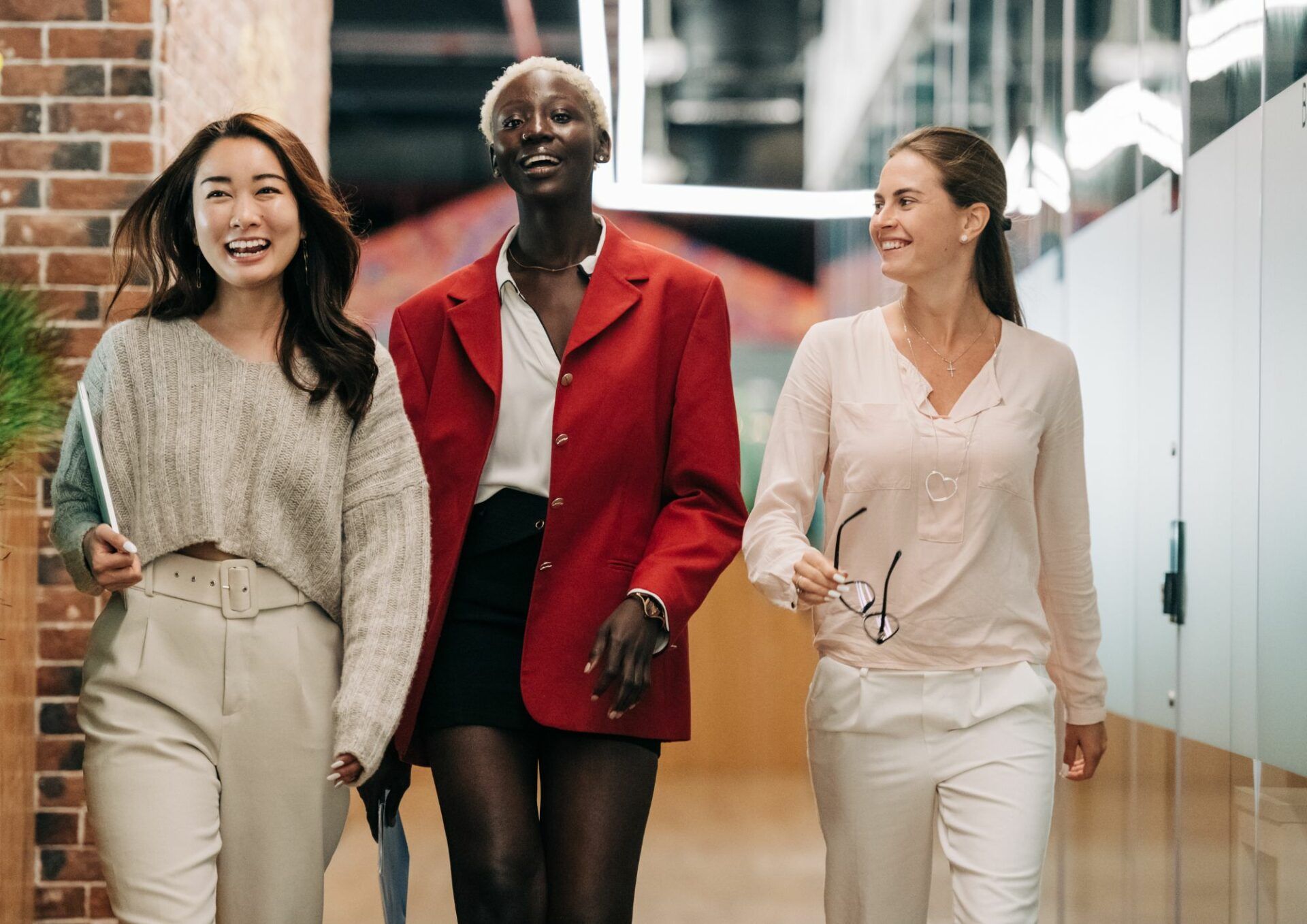 Tre skrattande kvinnor går bredvid varandra i en korridor.