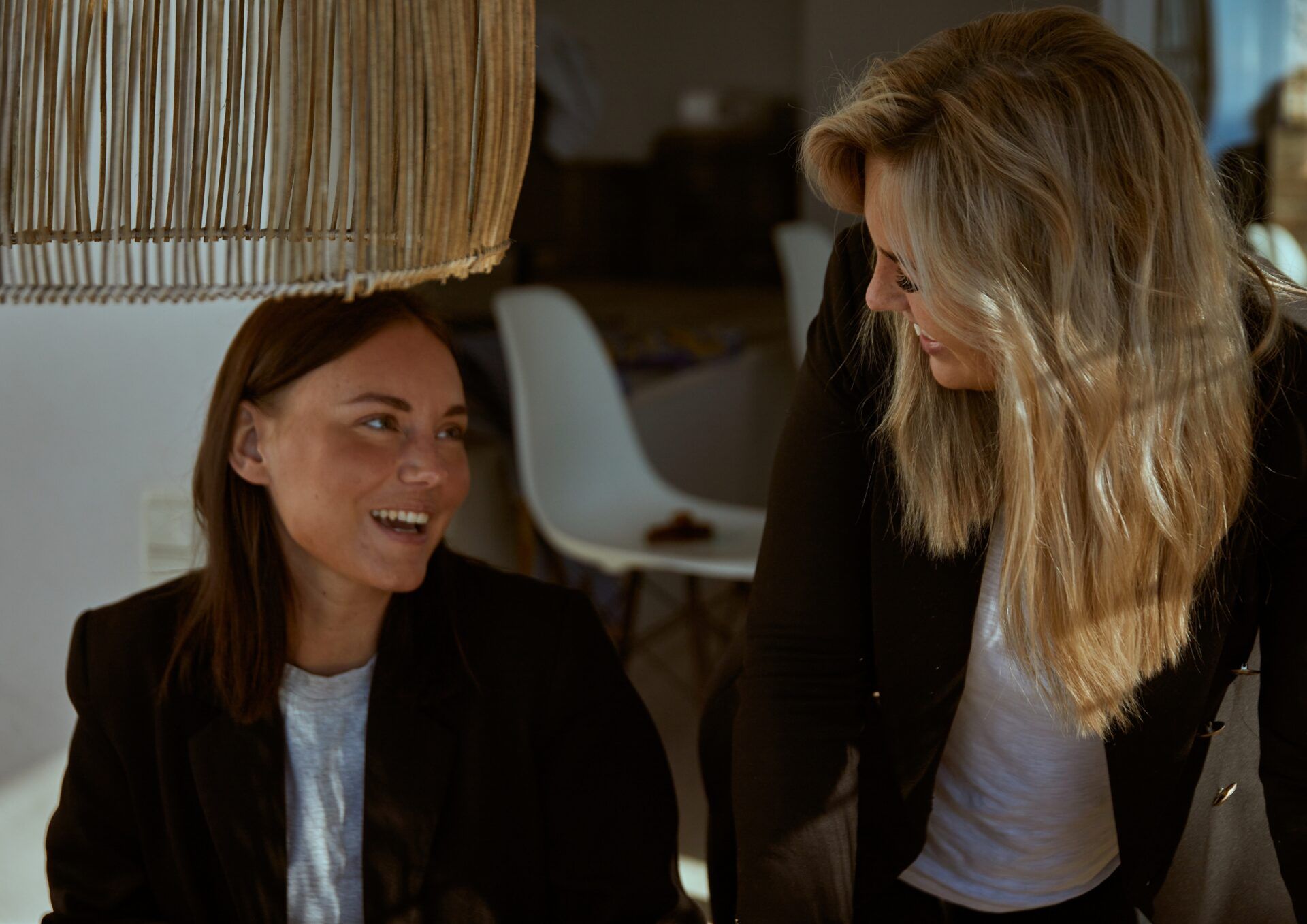 Martina Myrén och Madeleine samtalar och ler mot varandra i en inomhusmiljö