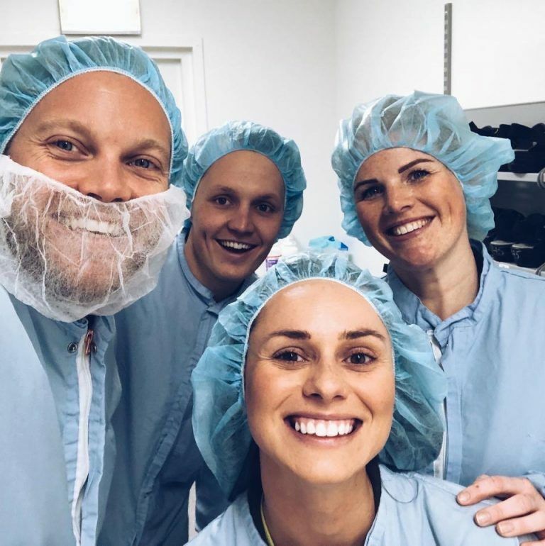 Gruppbild på nära håll av medarbetare på AztraZeneca och representater från Oddwork. Alla är klädda i ljusblå skyddskläder och skyddsmössor för håret.