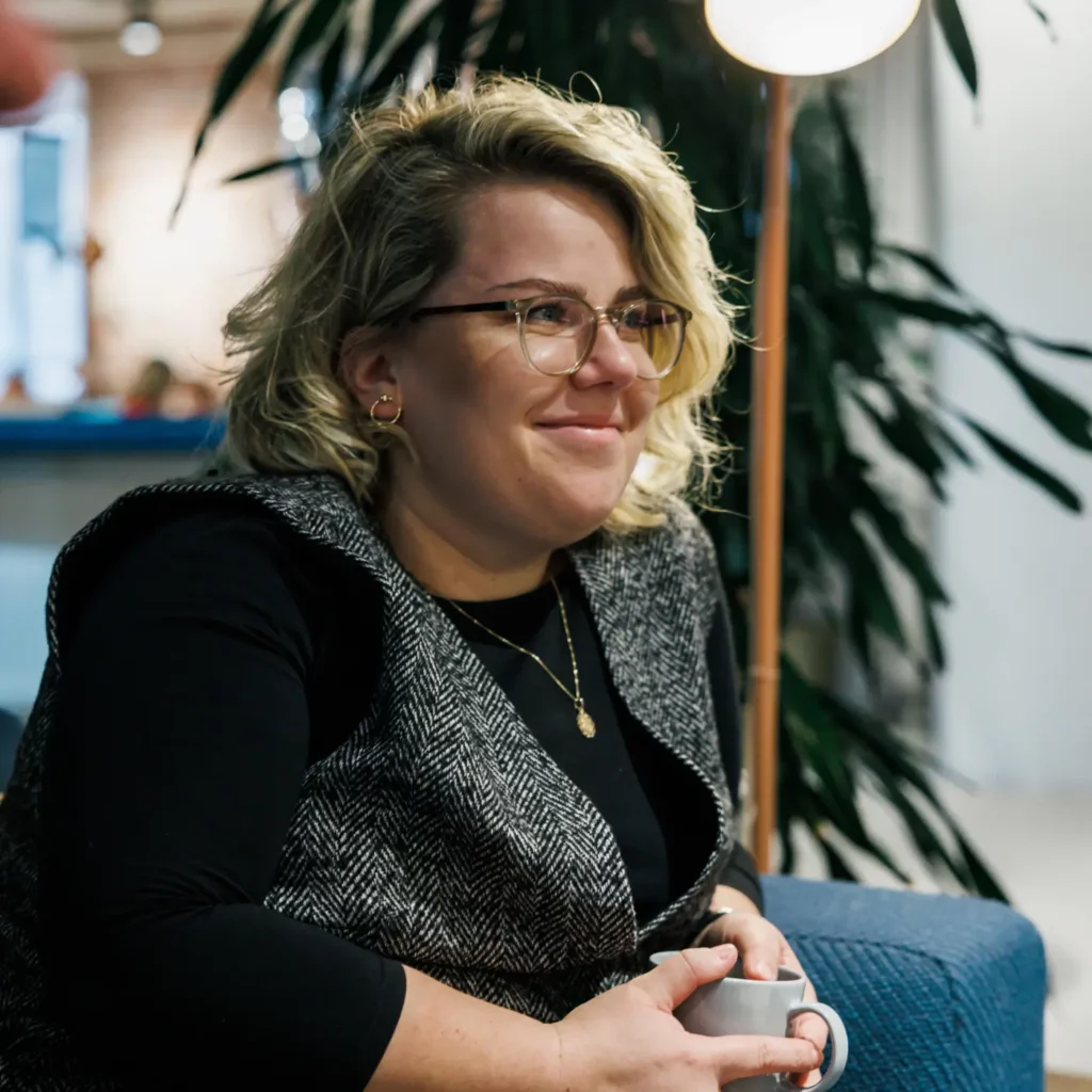 Person med glasögon som tittar till höger och håller en kaffekopp i händerna