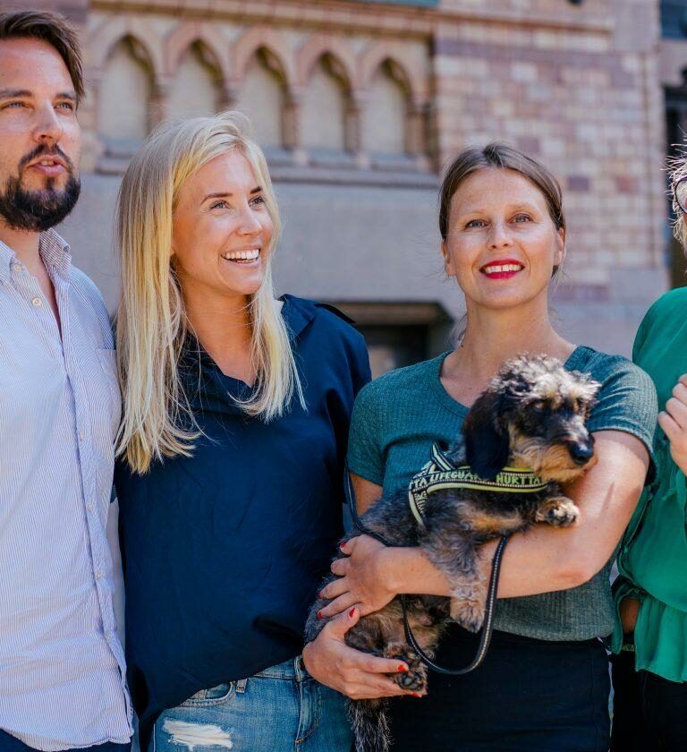 Foto på fyra anställda på Wint samt deras kontorshund. Gruppen står utanför Wints kontor en solig sommardag.