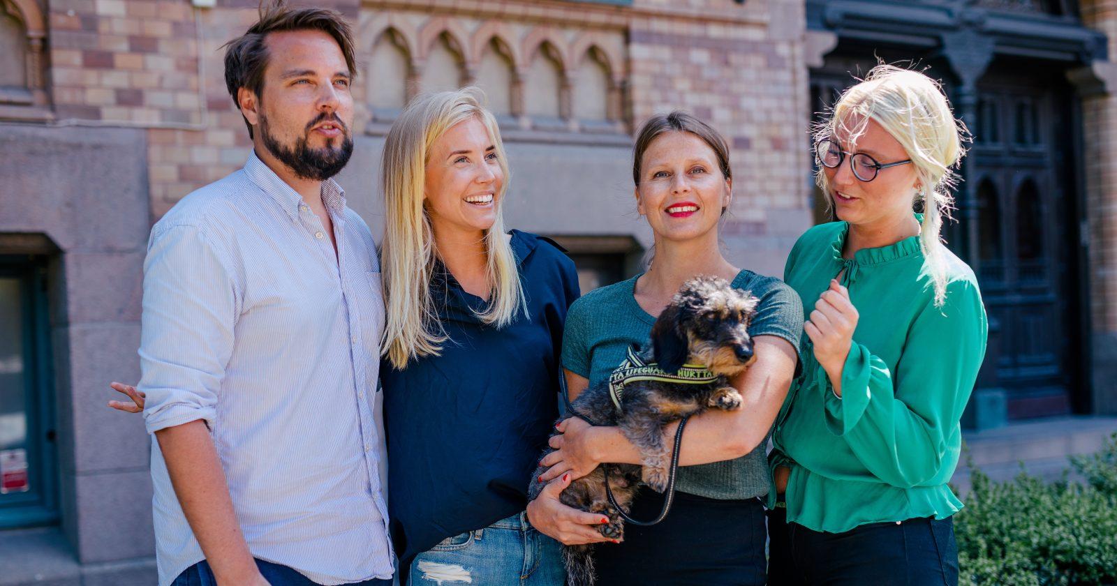 Foto på fyra anställda på Wint samt deras kontorshund. Gruppen står utanför Wints kontor en solig sommardag.